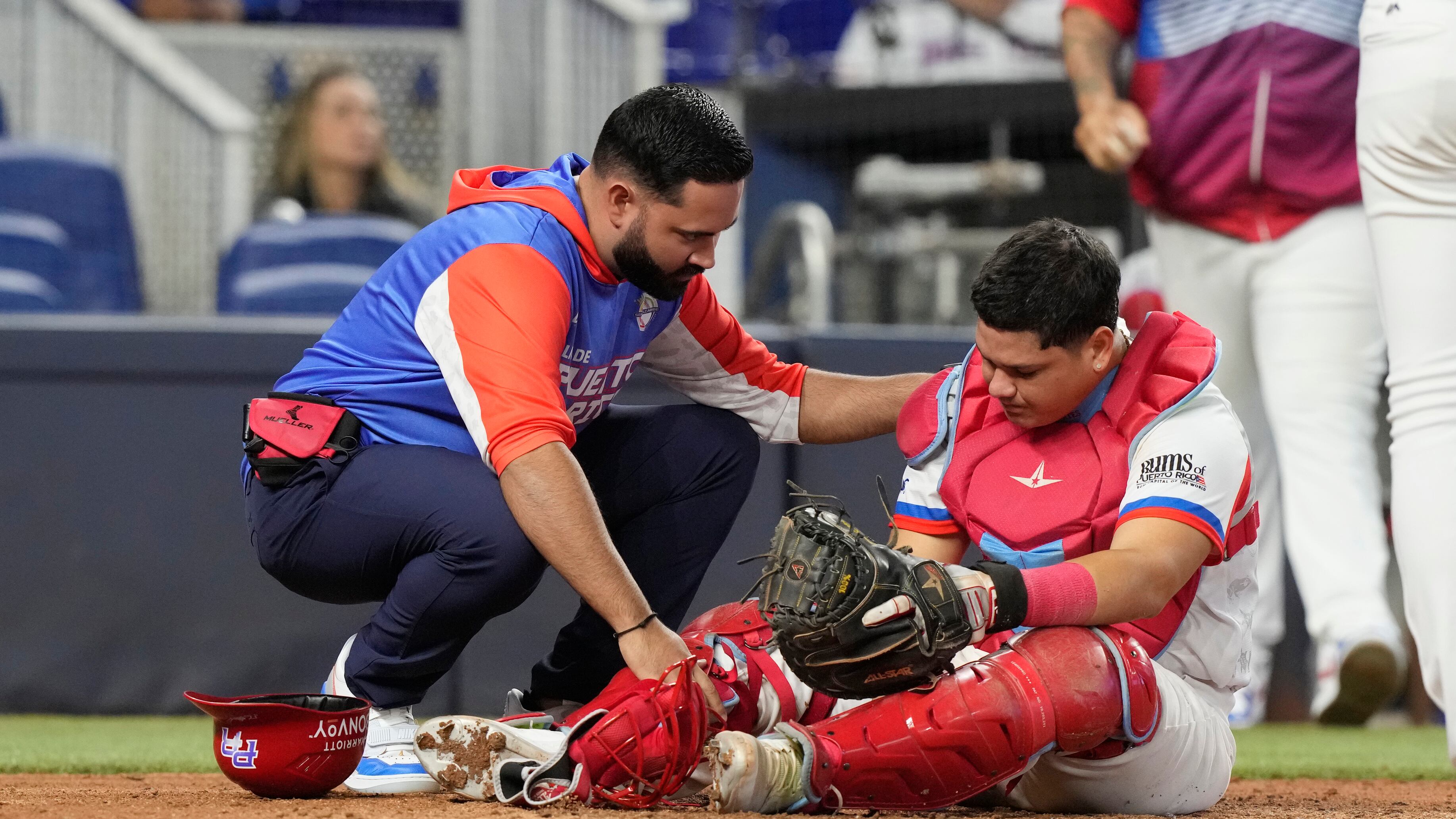 El receptor de Puerto Rico, Jonathan Morales, es atendido por un entrenador después de que fue golpeado por un lanzamiento durante la séptima entrada de un juego de béisbol de la Serie del Caribe contra Curazao, el miércoles 7 de febrero de 2024, en Miami. Curazao derrotó a Puerto Rico 2-0. (Foto AP/Marta Lavandier)