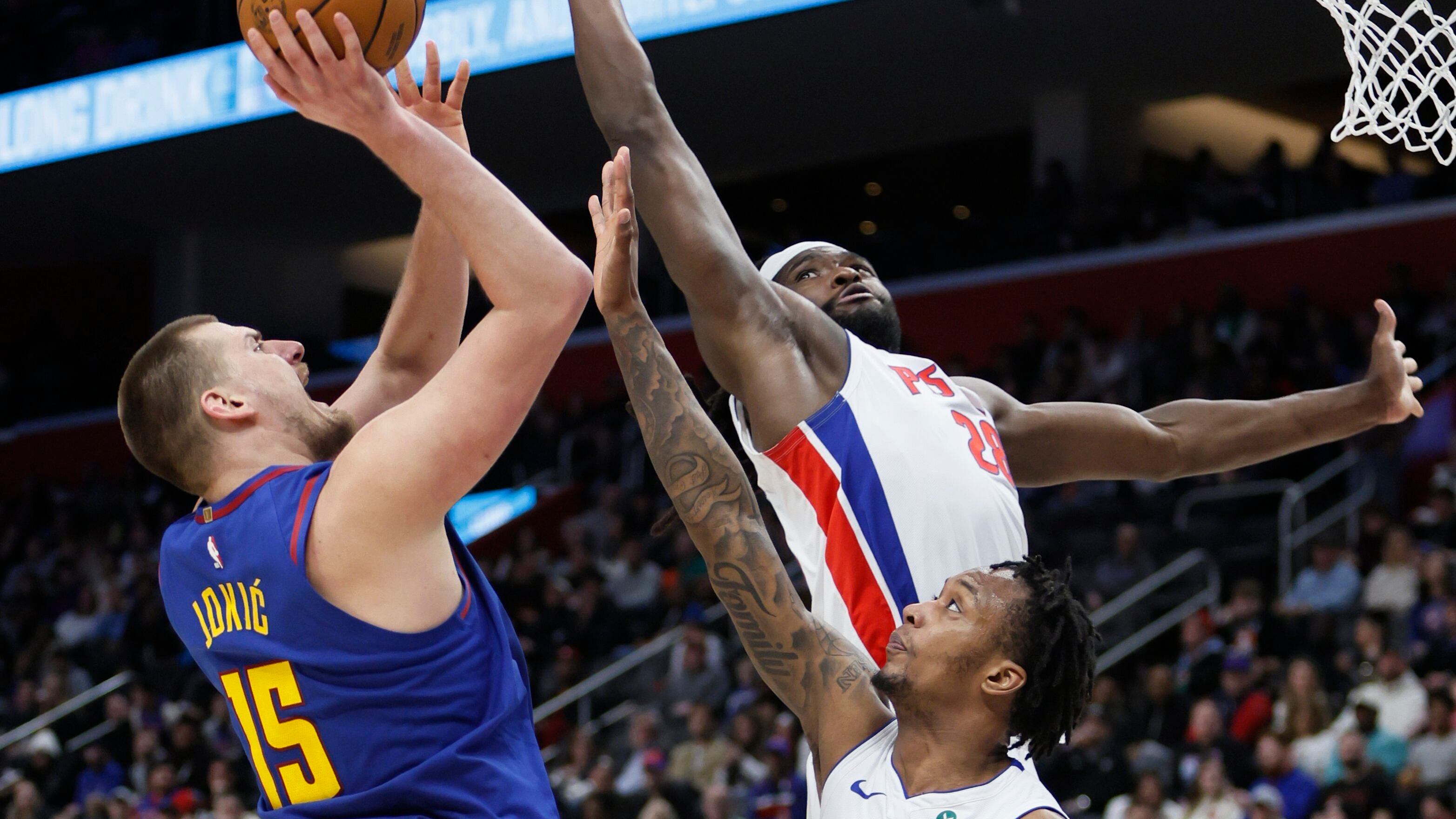 El pívot de los Denver Nuggets, Nikola Jokic (15), es defendido por el pívot de los Detroit Pistons, Isaiah Stewart (28), y el alero Ronald Holland II (00), mientras realiza un tiro durante la primera mitad de un partido de baloncesto de la NBA el viernes 28 de febrero de 2025 en Detroit. (Foto AP/Duane Burleson)