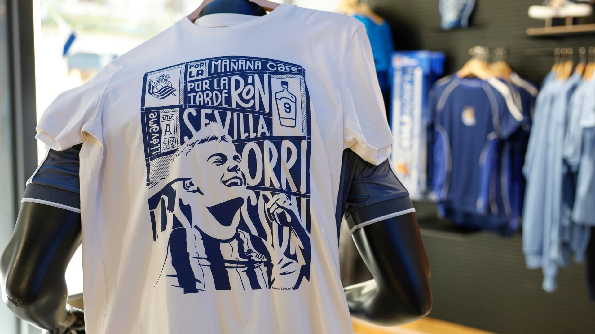 La Real Sociedad ha apelado directamente al corazón de la afición, siguiendo una estrategia de marketing con lemas y jugadores que son emblemas e iconos para los seguidores txuri urdin. La adaptación del tema 'Café con ron' de Bad Bunny protagonizada por el delantero islandés Orri Óskarsson se ha convertido en una de las camisetas más vendidas del 'merchandising' diseñado por la Real Sociedad para la final de La Copa del Rey. EFE/Juan Herrero.