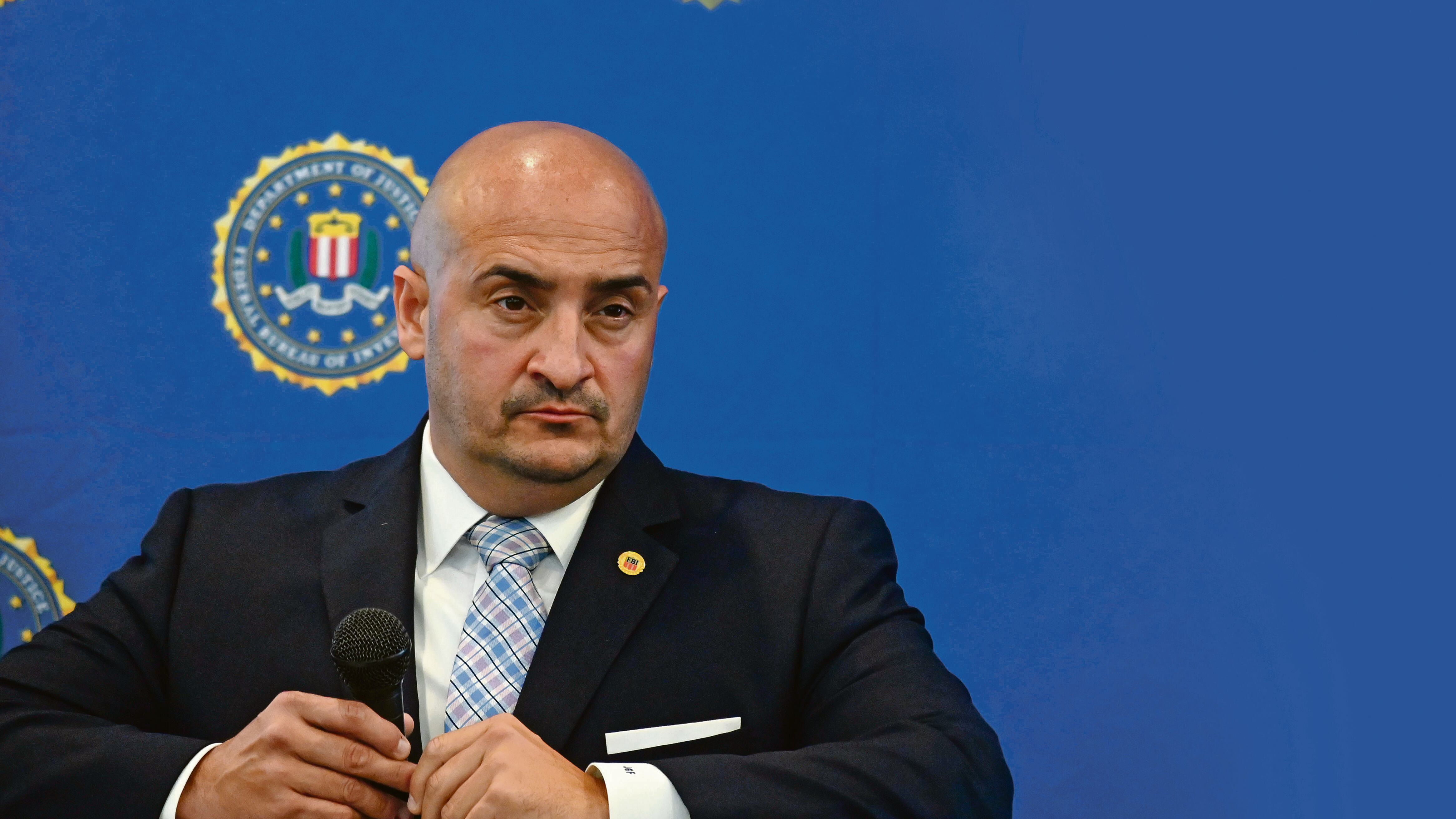 Joseph González mira fijamente a un miembro de la prensa durante una conferencia. Sostiene un micrófono en su mano.