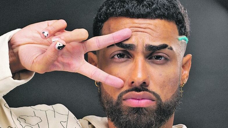 Jay Wheeler hace un signo de paz con su mano derecha sobre su cara, la palma hacia la cámara y los dos dedos enmarcando uno de sus ojos.